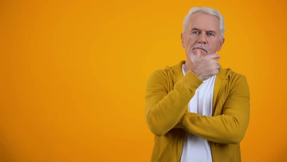 Senior Man Touching Chin, Thinking About Decision Against Orange Background