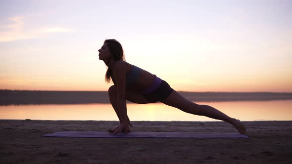 A Sports Brunette Doing Stretching Exercises on a Mat on the Beach or a Lake