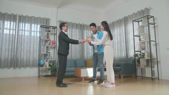 Asian Couple Receiving The House Model From A Real Estate Agent While Standing In The House For Sale