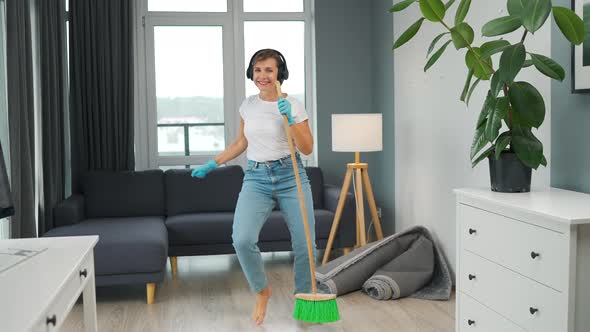 Woman in Headphones Cleans the House and Have Fun Singing with a Broom Like a Star at a Concert