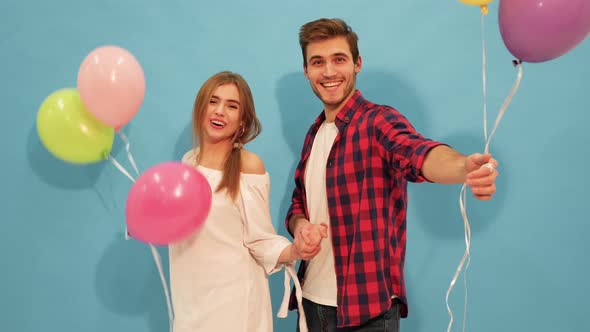 Smiling Beautiful Girl and her Handsome Boyfriend holding bunch of colorful air balloons