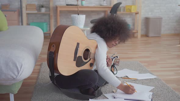 African American Woman with an Afro Hairstyle Composes a Song and Plays the Guitar Sitting on the