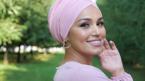 Young Muslim Woman in Headscarf Smiling on Background of Green Grass and Trees