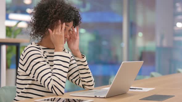 African Woman with Laptop Having Headache in Office