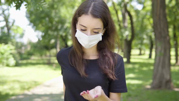 A Young Turkish Woman in a Face Mask Applies Disinfection Gel on Her Hands and Looks at the Camera