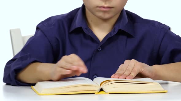 Boy Sits at the Table Leafing Through the Pages of a Book. White Background. Close Up