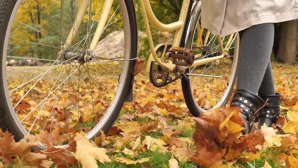 A Woman Walks Through an Autumn Park and Rolls a Bicycle and Kicks Autumn Yellow Leaves Closeup