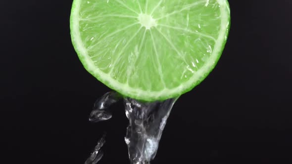 Water falling from juicy lime on black background. Lime slice and water splashing, drops of juice