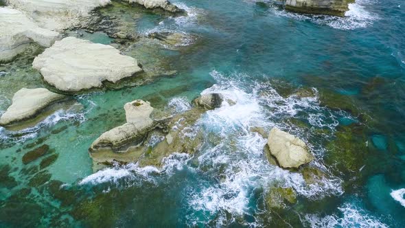 Aerial View of Waves Break on Rocks in a Blue Ocean