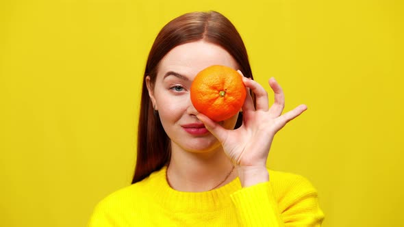 Closeup of Cheerful Redhead Charming Woman Closing One Eye with Tangerine and Smiling