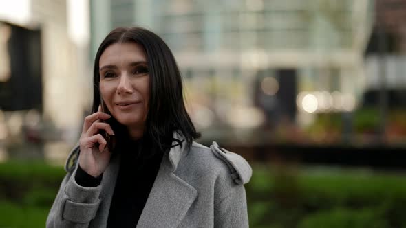 Adult Brunette Woman is Talking By Cell Phone Outdoors in City Center