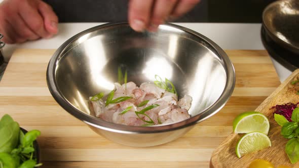 Professional Chef Adding Greenery to Raw White Fish Fillet in Metal Bowl on Cutting Board Closeup