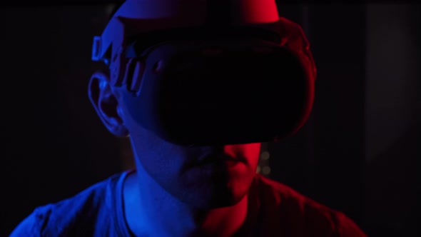 Young Man Plays a Game in a VR Helmet Under RedBlue Light