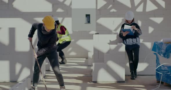 Female Construction Worker Brooming Near Coworkers