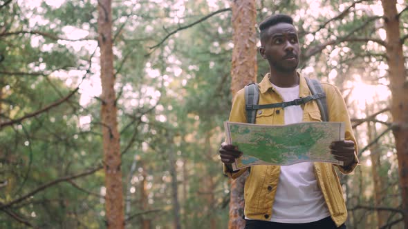 Smiling African American Man Is Walking in Forest Looking at Map Searching for Desired Tourist