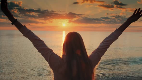 Young Woman with Outstretched Arms Enjoying the Beauty of Sunset on the Sea