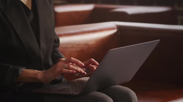 Unrecognisable Woman Dressed in a Modern Suit Sitting on a Leather Sofa and Typing