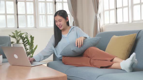 Asian Female Use Laptop Computer In Living Room While Lying On Sofa