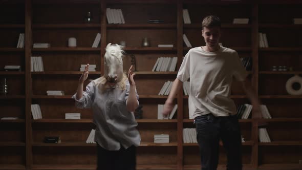 Young Man and Woman in Unicorn Mask Dancing and Having Fun in Library at Home