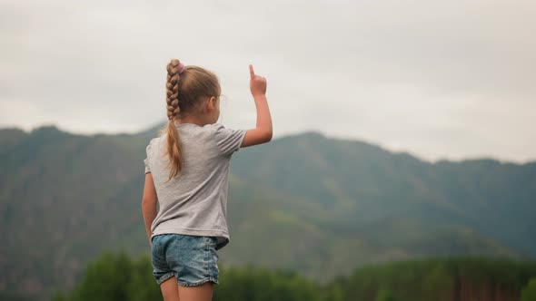 Little Child Girl with Braided Hair Points to Mountains