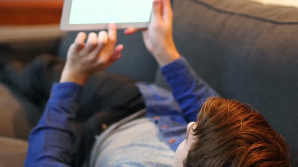 Man lying on sofa and using digital tablet in living room