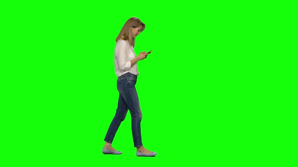 Blonde Woman Calmly Walking and Texting Message Vie Her Mobile Phone on Greenscreen. Chroma Key