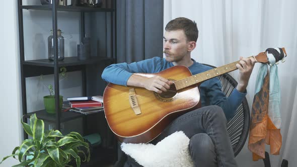 Young male solo guitarist playing acoustic guitar at modern home studio.