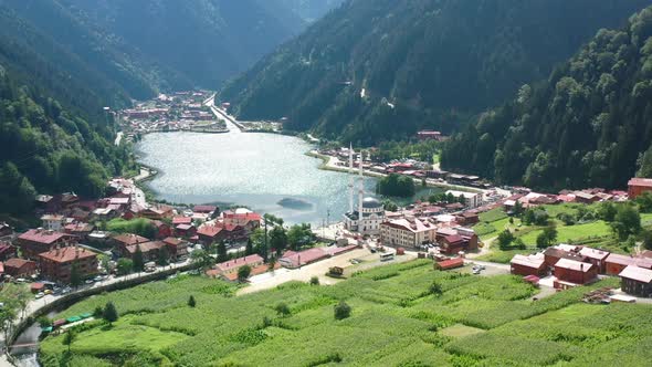 aerial drone flying backwards revealing the village below as the sun reflects off the lake surrounde