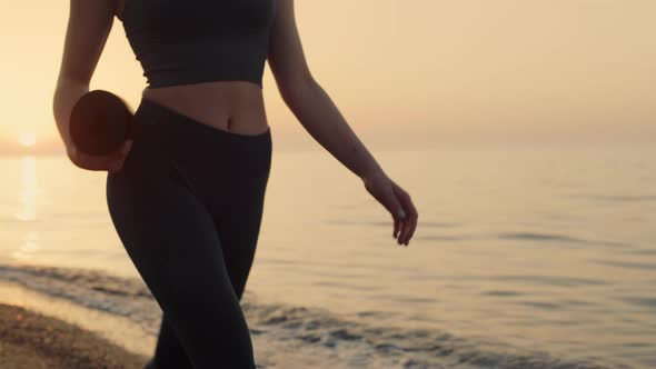 Fit Girl Holding Mat Walking Seashore at Sunset