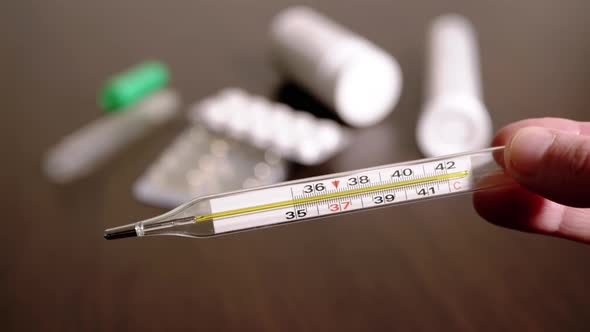 Female Hands Holding a Glass Mercury Thermometer with a High Body Temperature