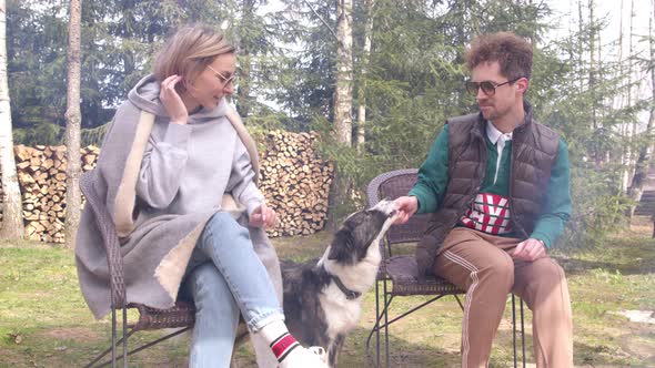 Beautiful Woman and Man Sitting By Campfire Plays with Dog Having Fun on Picnic