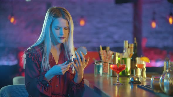 Gorgeous Young Woman Sitting By the Bartender Stand and Applying Red Lipstick on Her Lips