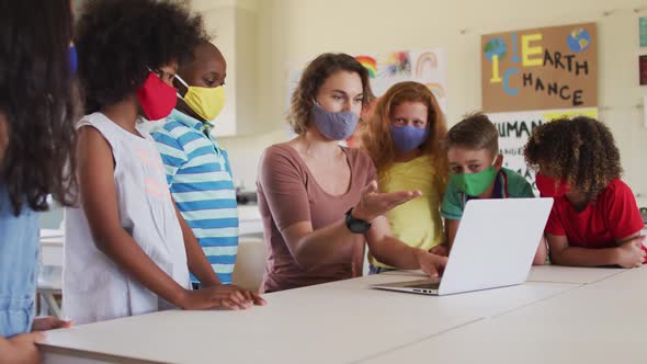 Female teacher wearing face mask using computer to teach kids in the class at school