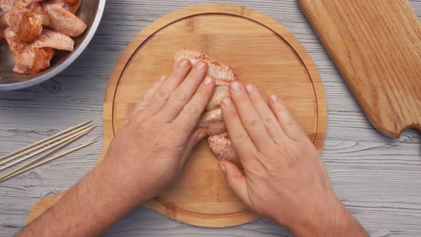 Hands are Placing Chicken Wings on a Board and Piercing It with a Wooden Skewer
