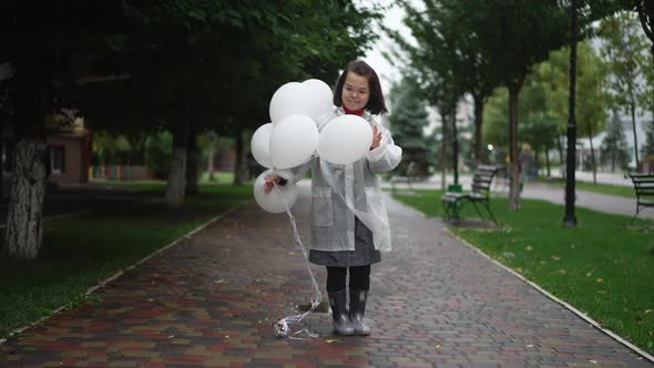 Wide Shot Portrait of Happy Confident Little Person in Rain Coat Standing with Balloons Outdoors