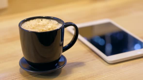Digital tablet and coffee cup on wooden table.