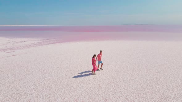 Aerial Drone Footage of Happy Young Couple in Pink Wear Having Fun and Joyfully Walking on White