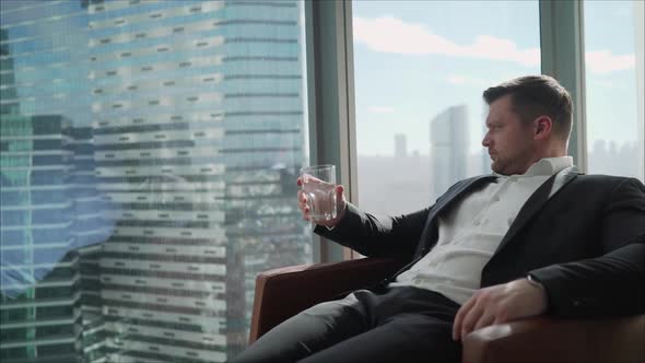 Handsome Businessman Relaxing on an Armchair Holding a Glass of Water in His Hand