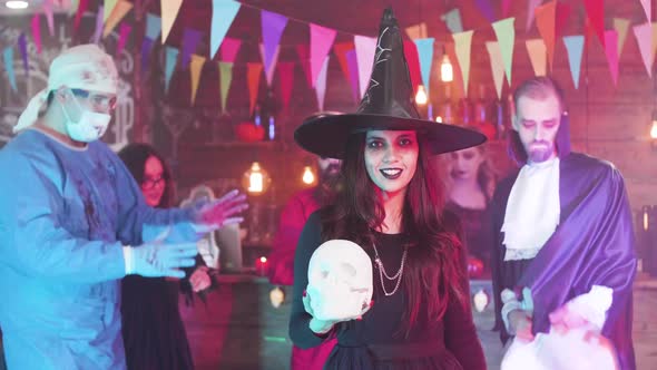 Young Woman Disguised in Witch Costume Hold a Skull in Her Hands at a Halloween Party