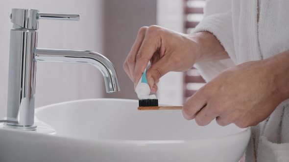 Closeup of Male Hands in Bathrobe Holding Bamboo Wooden Dental Tally Squeezing Out Tube of Whitening