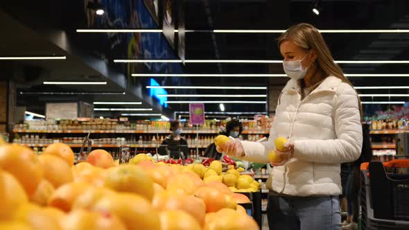 A Woman in a Supermarket Picks Fresh Oranges in Rubber Gloves