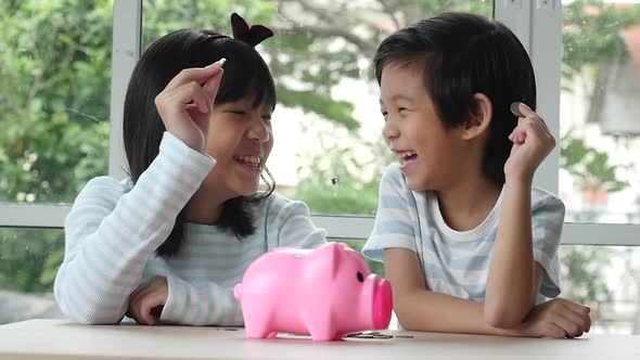 Cute Asian Child Putting A Coin Into A Piggy Bank