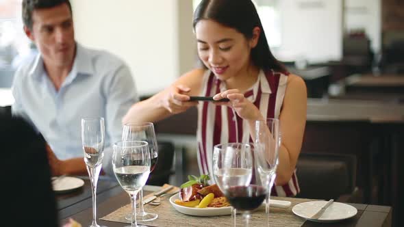 Woman dining in restaurant, photographing her food with a smartphone