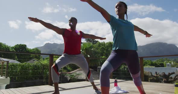 Relaxed biracial couple on terrace, practicing yoga together on mats