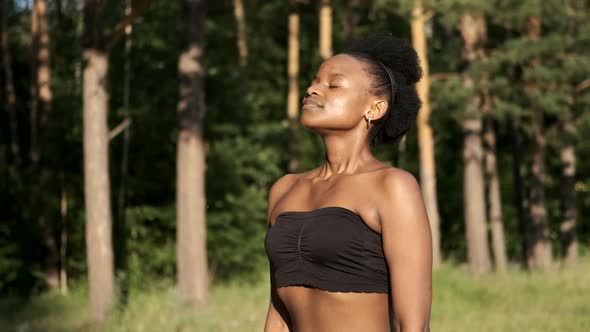 Calm Young Black Woman Taking a Deep Breath of Fresh Air, Relaxing, Meditating with Her Eyes Closed