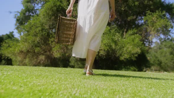 Back View Woman in White Boho Dress with Picnic Basket Walking in City Park 6K