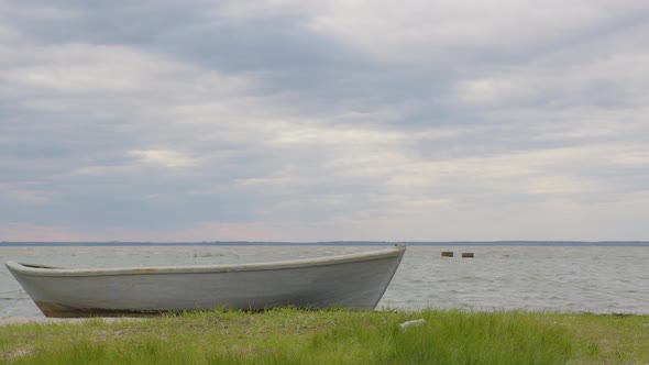 A Wooden Fishing Boat Moored on a Sandy and Grassy Shore at Sunset with a Cloudy Sky Time Lapse