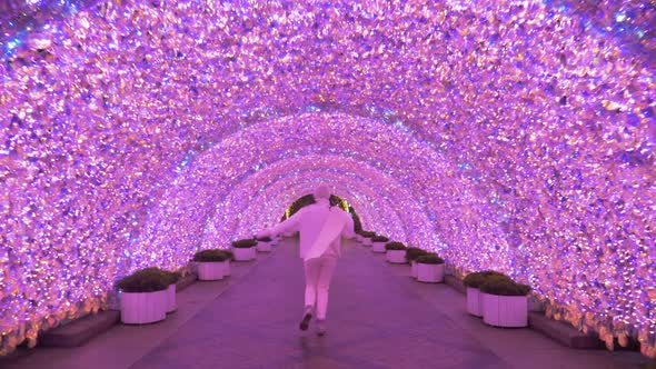 Woman in a White Sweater and Hat Walks Through a Pink Glowing Tunnel at Night