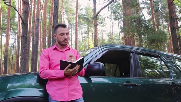 Pensive Businessman Sitting on the Hood Meditates and Makes Notes in a Notebook