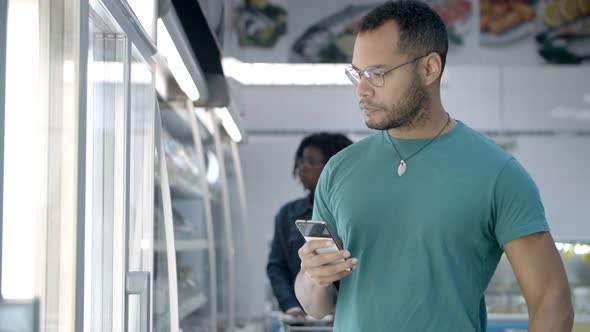 Focused African American Man Reading Shopping List on Smartphone